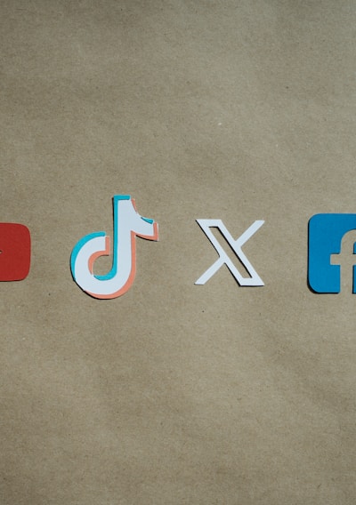 Four social media platform logos are arranged on a brown background. From left to right, the logos are for YouTube in red, TikTok in a combination of red, blue, and white, X in white, and Facebook in blue.